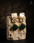 Gold and green earrings on a stone block with a dark background