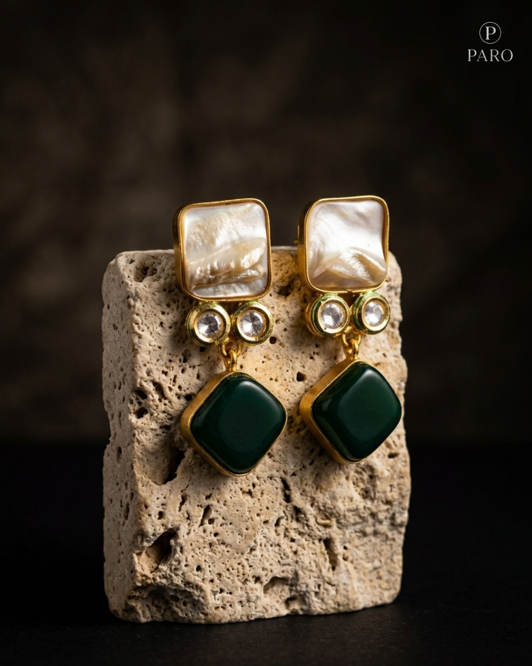 Gold and green earrings on a stone block with a dark background
