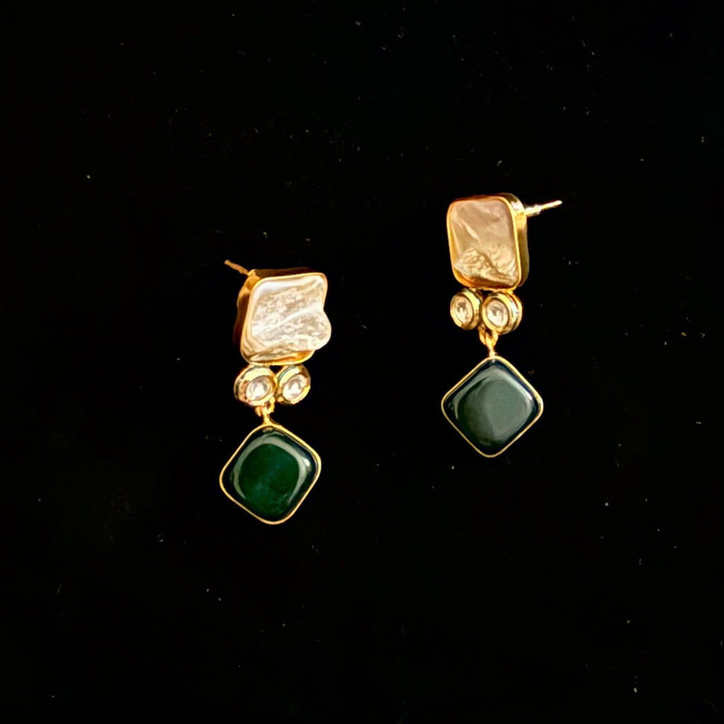 Pair of gold earrings with green and clear stones on a black background